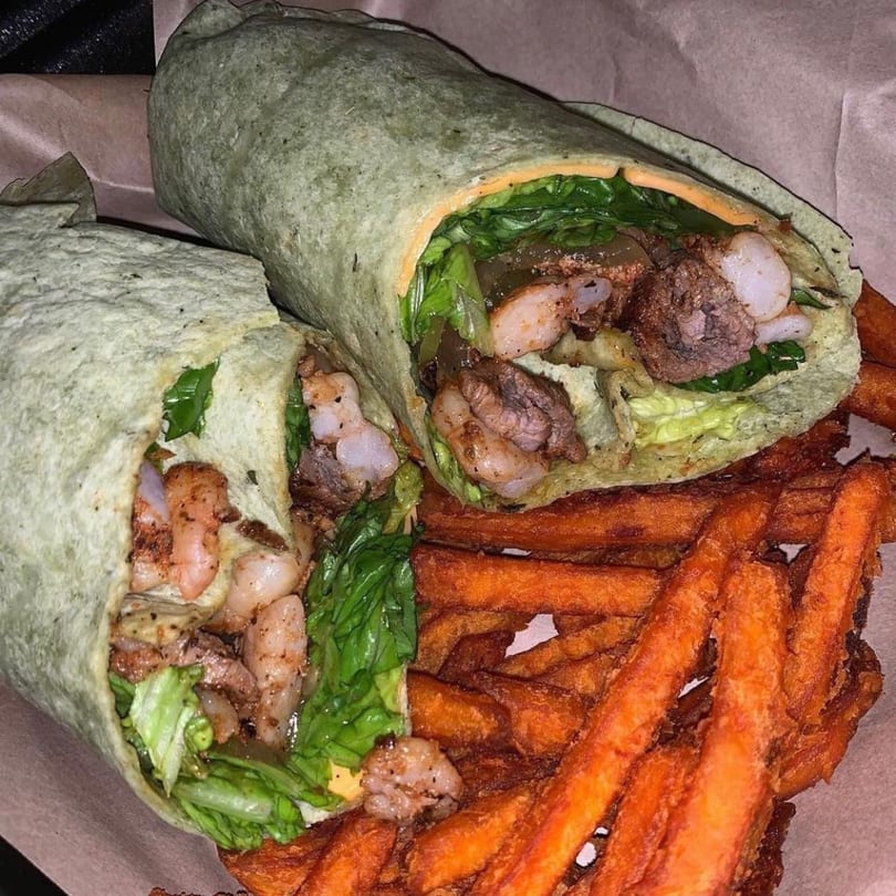 Two wraps filled with shrimp, steak, and lettuce, served with a side of sweet potato fries.