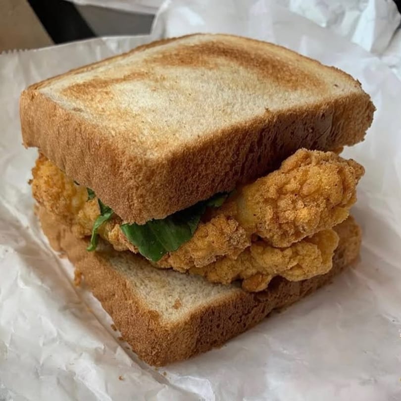 Smiley's Grill fried chicken sandwich with lettuce on toasted white bread, wrapped in paper.