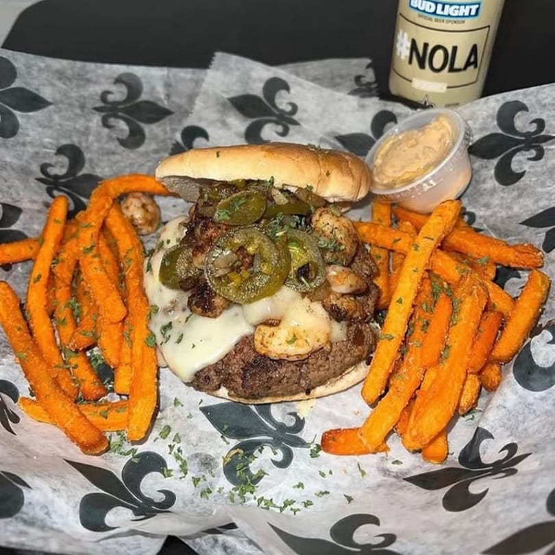 A Smiley's Grill burger with melted cheese, jalapeños, and shrimp, served with sweet potato fries.