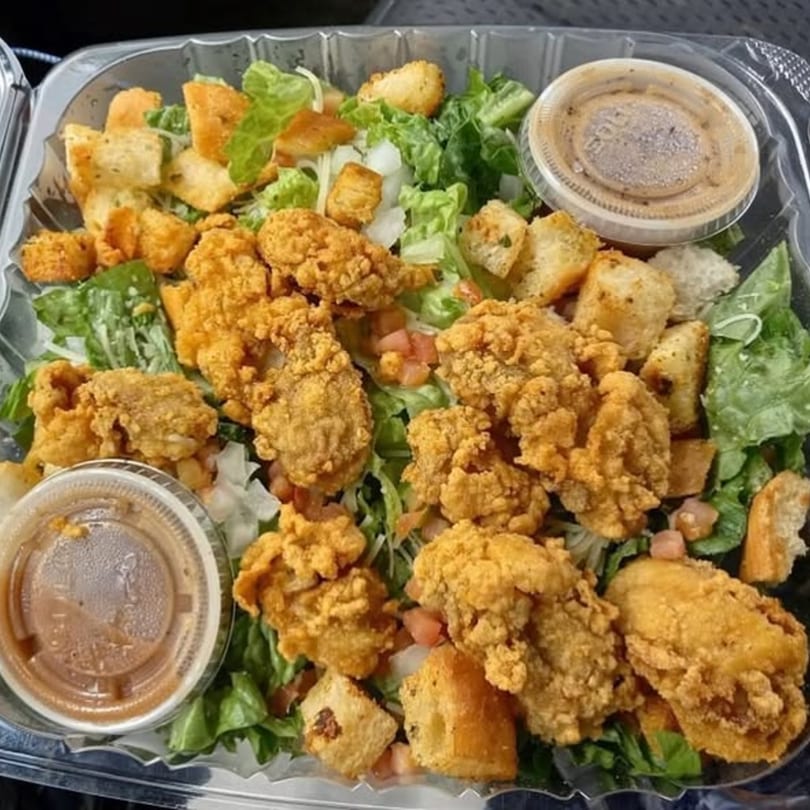 Smiley's Grill fried oyster salad with lettuce, croutons, tomatoes, and two dressing cups in a plastic container.