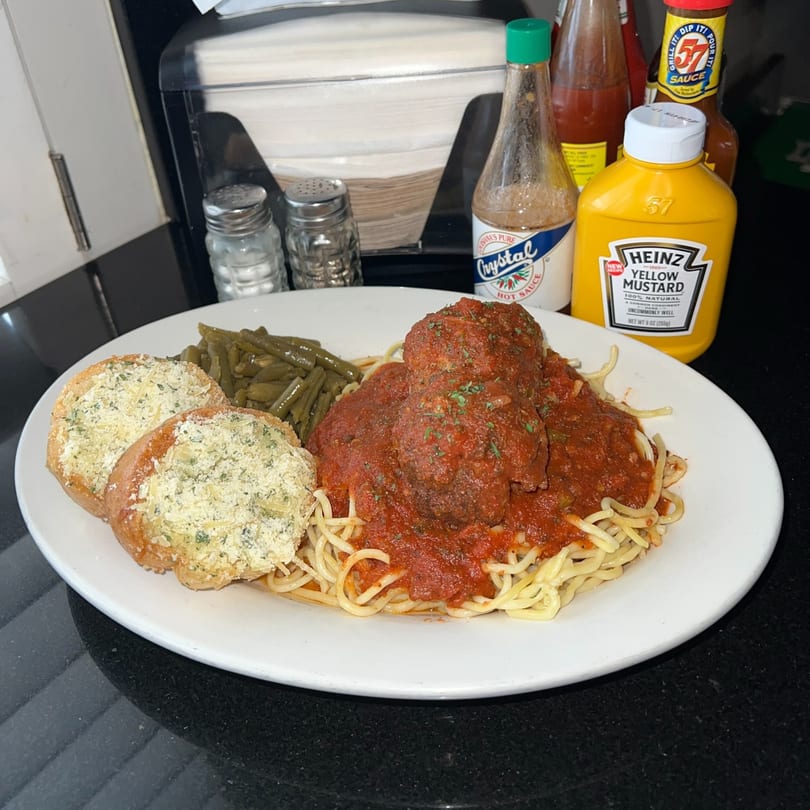 Spaghetti and meatballs with green beans and garlic bread, with condiments in the background.