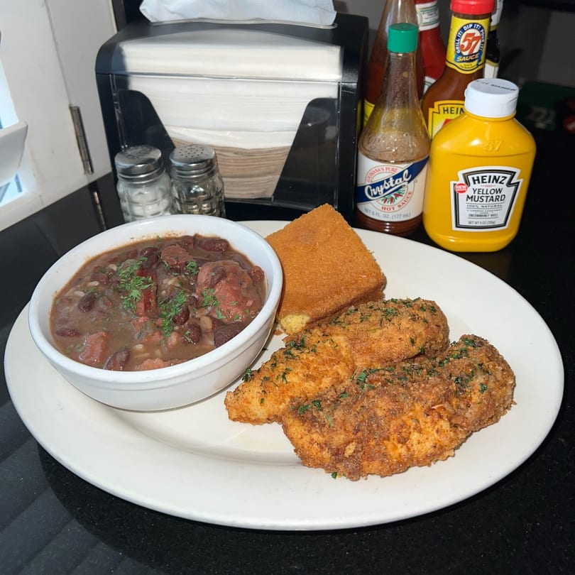 A plate of fried chicken, red beans and rice, and cornbread, with condiments in the background.